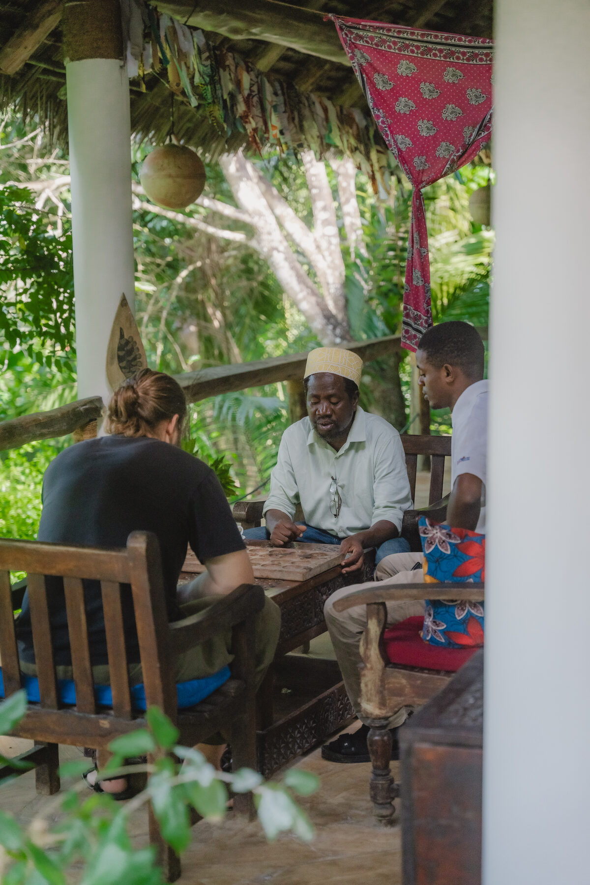 Guests and hosts gathered on a shaded veranda surrounded by tropical greenery